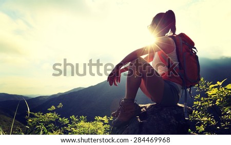 woman backpacker sit on sunrise mountain peak cliff rock enjoy the view