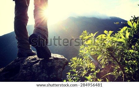 woman hiker legs climbing on sunrise mountain peak rock