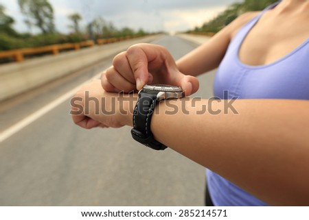 young woman jogger ready to run set and looking at sports smart watch, checking performance or heart rate pulse trace. Sport and fitness outdoors in city.