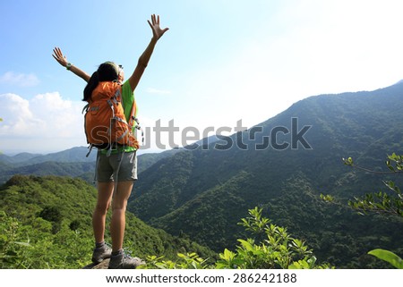 cheering woman hiker open arms at mountain peak cliff