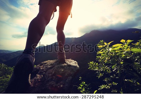 woman hiker legs climbing on sunrise mountain peak rock,vintage effect