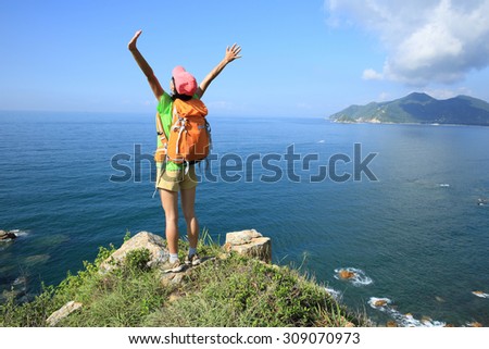 cheering young woman hiker open arms on seaside mountain peak
