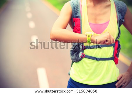 young woman jogger ready to run set and looking at sports smart watch, checking performance or heart rate pulse trace. Sport and fitness outdoors on forest trail.