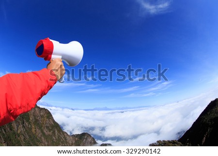 people hand hold loudspeaker to blue sky on mountain peak