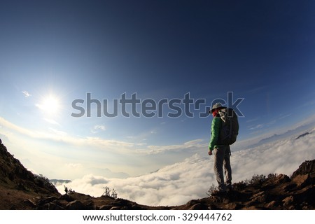young woman hiker looking at the beautiful rolling clouds and mountain landscape on peak