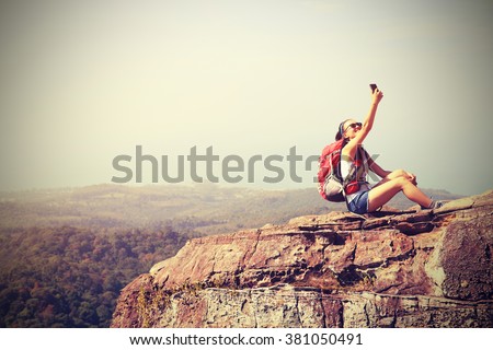 young woman backpacker taking photo with cellphone on mountain peak