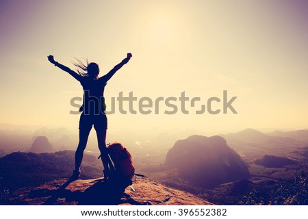 silhouette of cheering woman hiker open arms at mountain peak