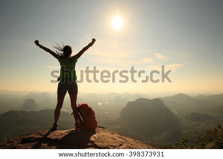 silhouette of cheering woman hiker open arms at mountain peak