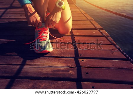 healthy lifestyle sports woman tying shoelace on wooden boardwalk sunrise seaside