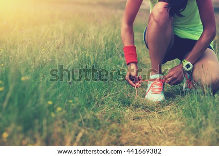 young woman runner tying shoelace on nature trail