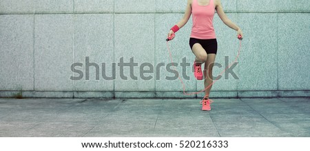 young fitness woman rope skipping against city wall
