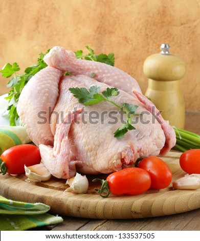 fresh raw chicken on a cutting board with vegetables and herbs