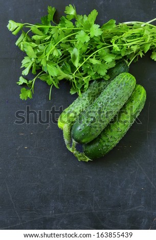 green cucumber with a bunch of parsley on a black wooden background