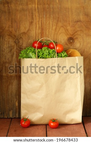 paper bag with food, lettuce, tomatoes, bread on a wooden background