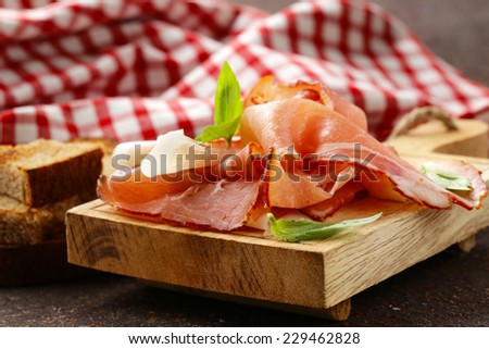 smoked ham jamon (Parma) with basil leaves on a wooden board
