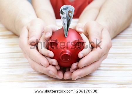 close up of father and son hands holding red piggy bank