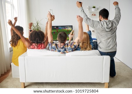 friendship, leisure and people concept - happy friends with non-alcoholic beer sitting on sofa and watching soccer or football game on tv at home