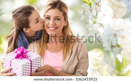 people, holidays and family concept - daughter kissing happy mother and giving her birthday present over cherry blossom background