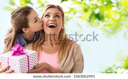 people, holidays and family concept - daughter kissing happy mother and giving her birthday present over green natural background
