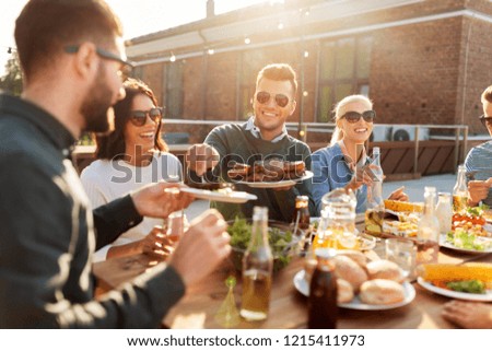 leisure and people concept - happy friends eating and drinking at barbecue party on rooftop in summer