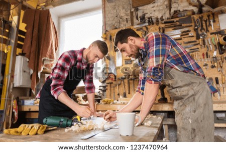 profession, carpentry, woodwork and people concept - two carpenters with ruler and blueprint at workshop