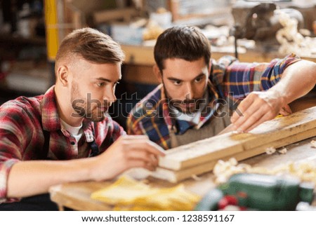profession, carpentry, woodwork and people concept - two carpenters measuring wooden board at workshop