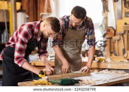 profession, carpentry, woodwork and people concept - two carpenters with ruler measuring wooden board at workshop