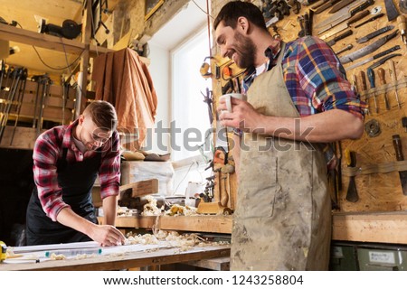 profession, carpentry, woodwork and people concept - two carpenters with ruler measuring blueprint and drinking coffee at workshop