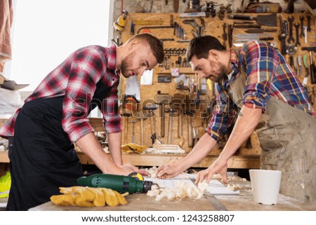 profession, carpentry, woodwork and people concept - two carpenters with ruler measuring blueprint at workshop