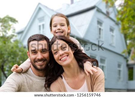 family, real estate and accommodation concept - happy mother, father and little daughter over house background