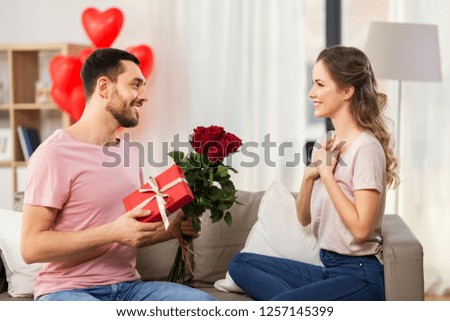 valentines day, couple, relationships and people concept - happy man giving woman flowers and present at home