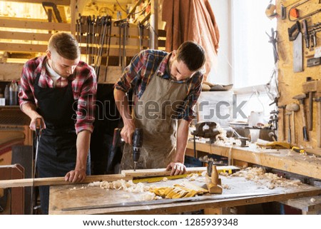 profession, carpentry, woodwork and people concept - two carpenters with wooden board, saw and electric drill working at workshop