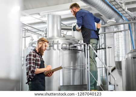 manufacture, business and people concept - men with clipboard and malt working at brewery or beer plant kettle