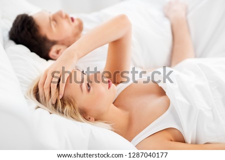 sleeping problems and people concept - unhappy woman lying in bed with snoring man