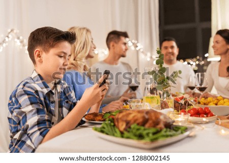 technology, holidays and people concept - happy boy with smartphone having family dinner party at home