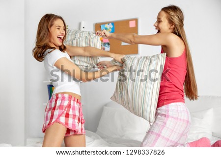 friendship, people and pajama party concept - happy friends or teenage girls having fun and pillow fight on bed at home