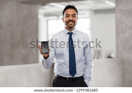 business, technology and people concept - smiling indian businessman with smartphone over office background