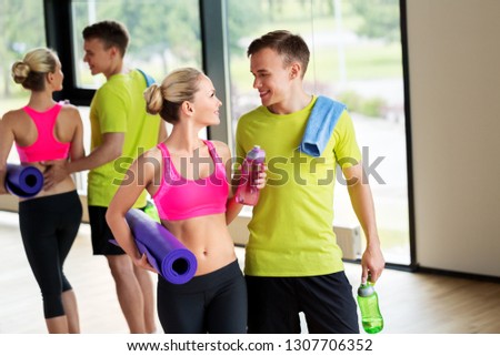 sport, fitness and people concept - smiling couple with water bottles, exercise mat and towel in gym