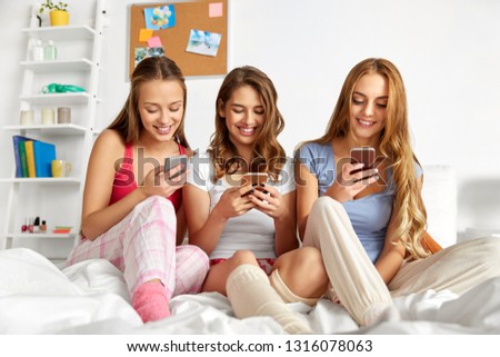 friendship, pajama party and technology concept - happy friends or teenage girls with smartphones at home