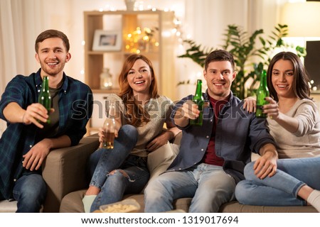 friendship and leisure concept - happy friends toasting non-alcoholic beer at home in evening