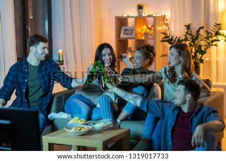 friendship, and leisure concept - happy friends with non-alcoholic drinks and snacks watching tv at home in evening