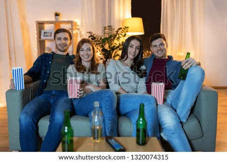 friendship and leisure concept - happy friends with non-alcoholic beer and popcorn watching tv at home in evening