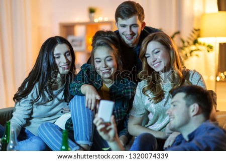 friendship, people, technology and entertainment concept - happy friends with smartphone and drinks watching tv at home in evening