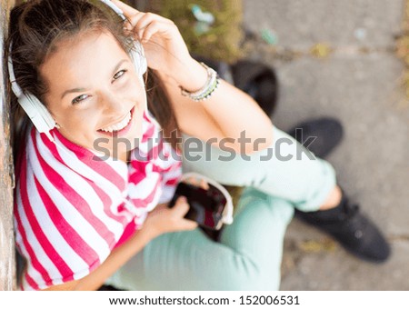 summer holidays and technology concept - teenage girl with headphones listening to music outside