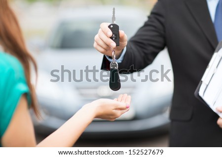 transportation and ownership concept - customer and salesman with car key outside