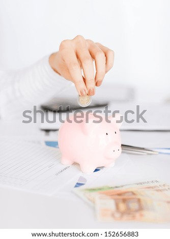 business, office, household, school, tax and education concept - woman hand putting coin into small piggy bank