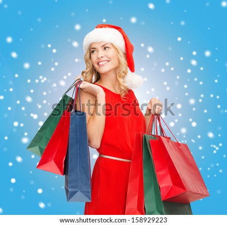 shopping, sale, gifts, christmas, x-mas concept - smiling woman in red dress and santa helper hat with shopping bags