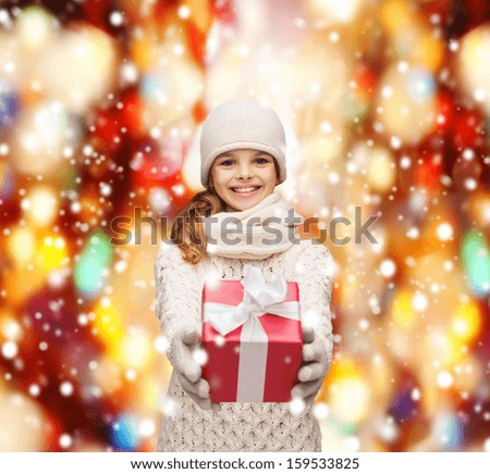 christmas, x-mas, winter, happiness concept - smiling girl in hat, muffler and gloves with gift box