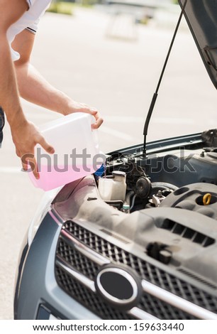 transportation and vehicle concept - man opening car bonnet and filling windscreen water tank with washing liquid