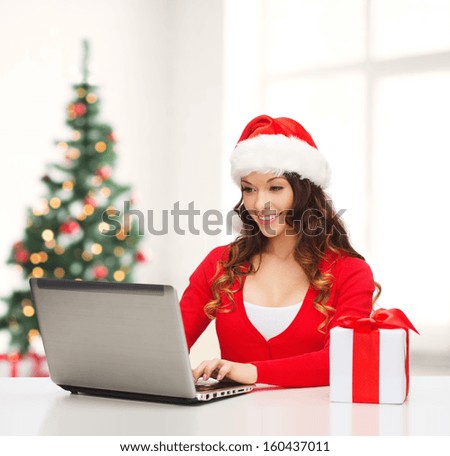 christmas, x-mas, online shopping concept - woman in santa helper hat with gift box and laptop computer